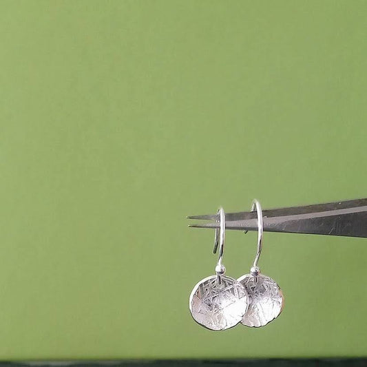 Silver earrings on a pair of tweezers against a green background